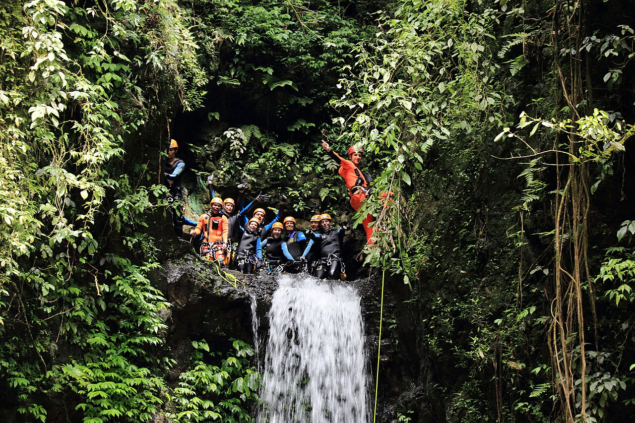 A canyoning group wearing helmets and harnesses above a waterfall